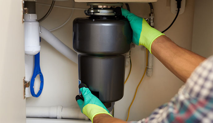 A professional of Chenal Restoration installing a garbage disposal unit under a kitchen sink