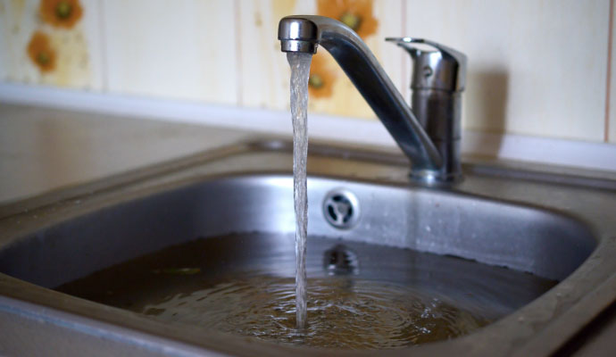 A stainless steel kitchen sink filled with water while a faucet continues to run