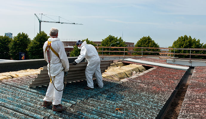 Two people are removing asbestos from roof
