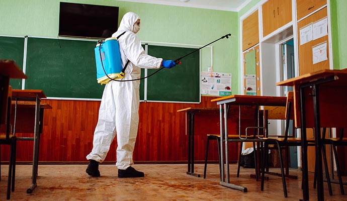 Professional performing classroom disinfection service wearing protective equipment and using a sprayer