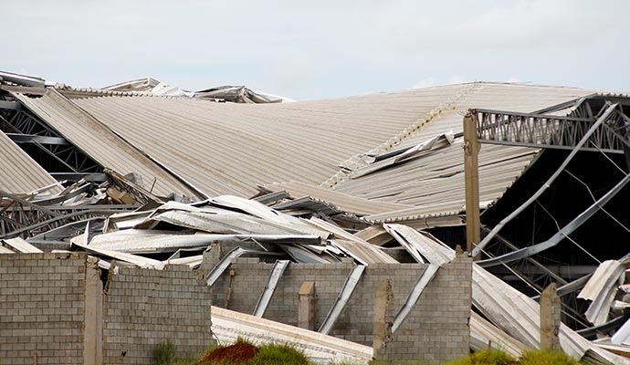 Damaged industrial facility with collapsed roof and concrete walls Industrial facility severely damaged with a collapsed metal roof and broken concrete walls after a disaster