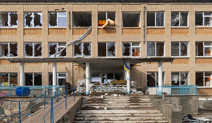 Damaged school building with shattered windows, broken facade and debris scattered at the entrance