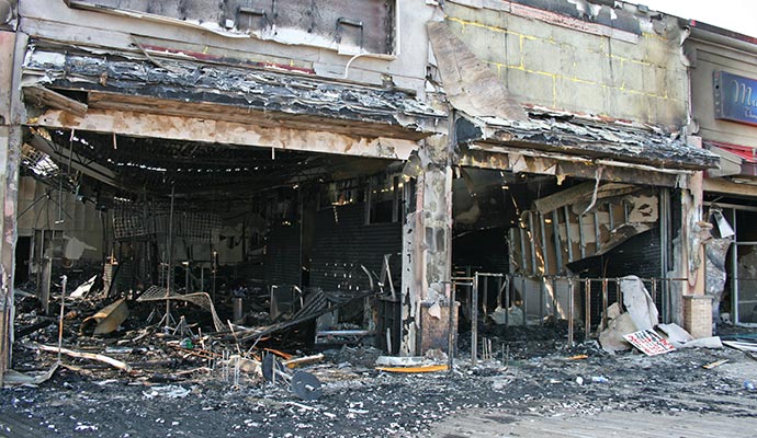 Fire-damaged commercial building with collapsed roof and charred walls Fire-damaged commercial building with a collapsed roof, charred walls and debris scattered across the entrance