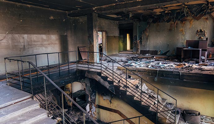 Interior of a burned building with charred walls, debris and a damaged staircase