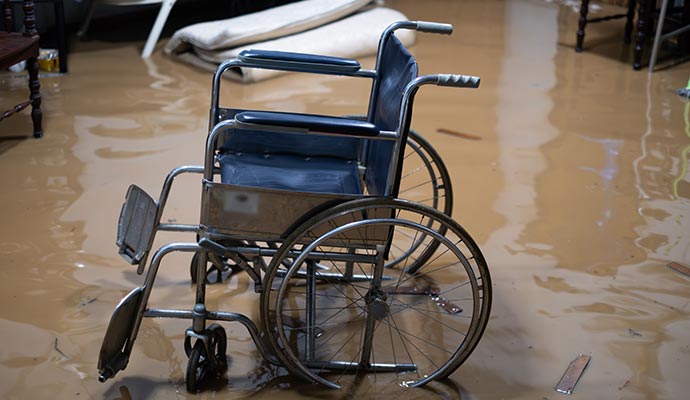 Flood-damaged hospital room showing a wheelchair in muddy water and scattered furniture