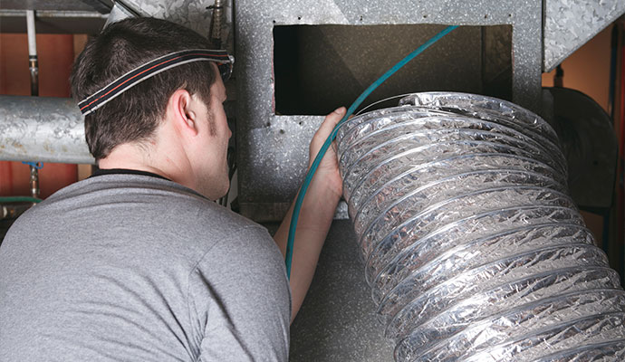 Technician guiding a hose into an HVAC duct system