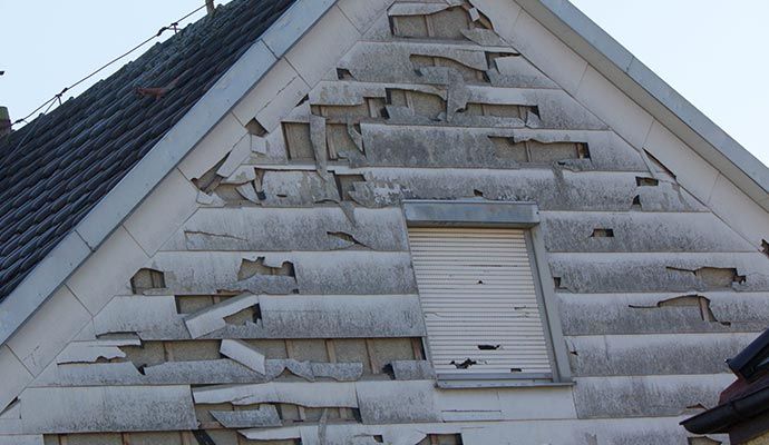 House exterior with hail-damaged siding Exterior siding of a house showing severe damage and peeling caused by hail