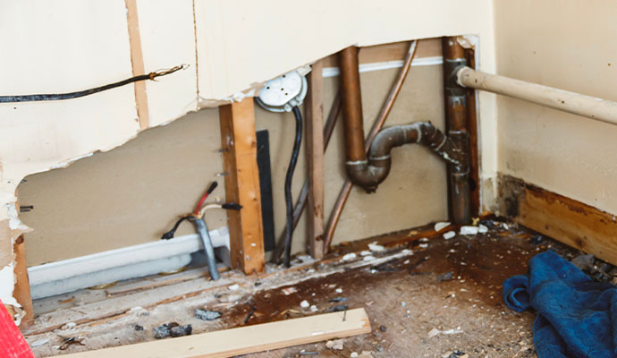 Leaked water pipe exposed behind damaged wall